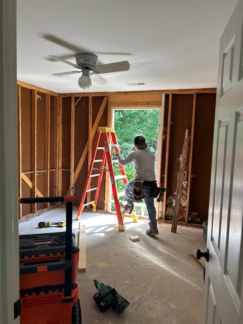 Worker stepping onto a ladder in front of window frame.